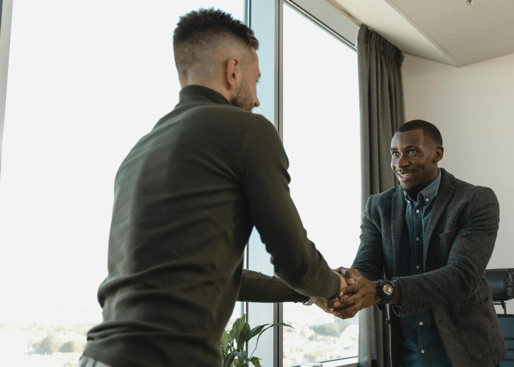Opportunities Two businessmen exchanging a handshake during a professional meeting in a modern office setting.